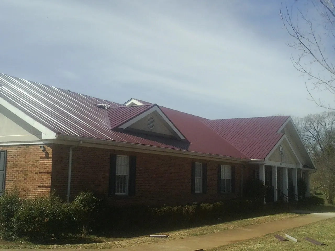 Red metal roof with gabled entries on a long brick building, from a Hail Damage Roof Repair job in Goshen